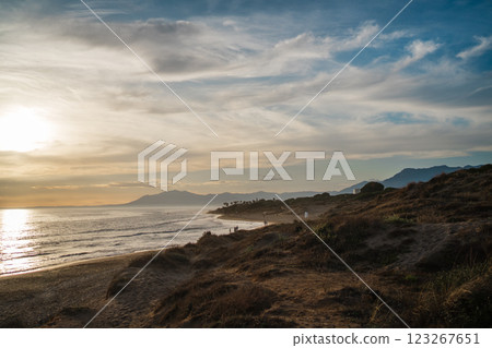 The golden light of sunset bathes the coastal dunes as distant mountains provide a stunning backdrop 123267651