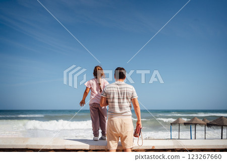 A father and daughter walk side by side along a sandy beach, enjoying a quiet moment together by the A father and daughter walk side by side along a sandy beach, enjoying a quiet moment together by the 123267660