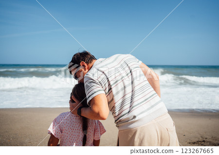 A father holds his daughter as they look out to the sea, enjoying the peaceful view and nature A father holds his daughter as they look out to the sea, enjoying the peaceful view and nature 123267665