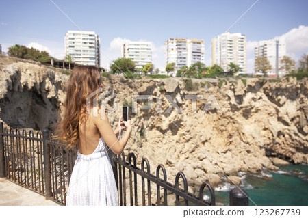Woman in summer dress taking photo of coastal cliffs Woman in summer dress taking photo of coastal cliffs 123267739