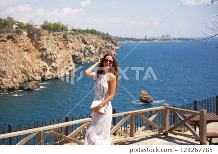Smiling woman in summer dress enjoying coastal cliff view  123267785