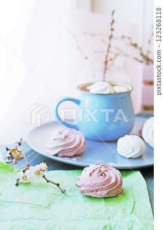 A cup of hot chocolate with marshmallows and a branch of blossoming apricot in a glass vase on a blue wooden table. 123268118