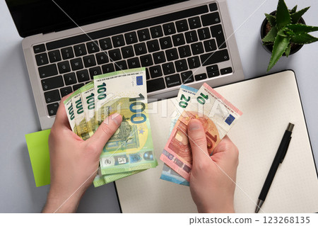 Hands counting euro banknotes over a notebook and notepad on an office desk. Idea passive income, remote work, digital business 123268135
