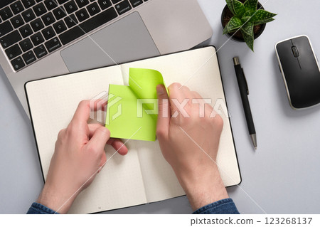 Hands peel off a green-colored sticker over an open notepad on a desk. A place for your text Hands peel off a green-colored sticker over an open notepad on a desk. A place for your text 123268137