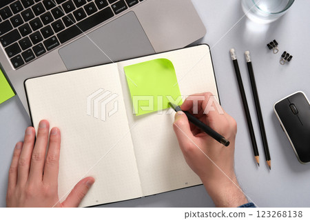Hand writing on a green colored post-it note above an open notepad on a desk. opyspace 123268138
