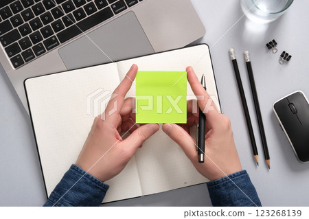 Hands holding a blank sticky note in green over an open notepad on a table. A place for your text 123268139