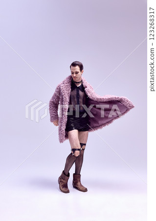 Full-length photo of man posing, dressed in striking leopard print coat and edgy accessories with bold gaze against sleek background. Full-length photo of man posing, dressed in striking leopard print coat and edgy accessories with bold gaze against sleek background. 123268317