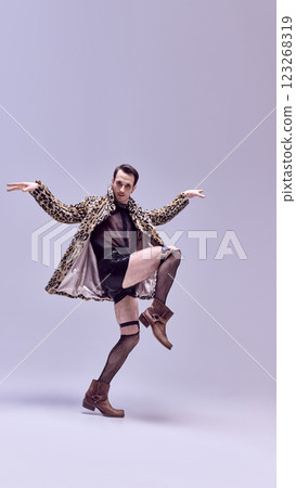 Expressive dancer, standing in stylish striking leopard print coat and edgy accessories with bold gaze against white background. Expressive dancer, standing in stylish striking leopard print coat and edgy accessories with bold gaze against white background. 123268319
