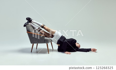 Dramatic performer, young man draped over chair with fluid body positioning and theatrical motion against white studio background. 123268325