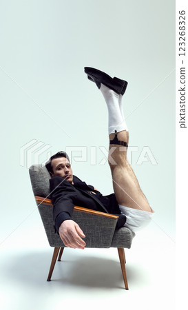 Artistic young man, stylish model lounging with extended leg and playful expression against white studio background. 123268326
