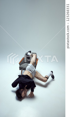 Creative young man, dance performer entangled in chair with expressive movement and artistic composition against white studio background. Creative young man, dance performer entangled in chair with expressive movement and artistic composition against white studio background. 123268331