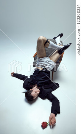 Fashion-forward young male model, collapsing dramatically with rose in hand against white studio background. Concept of beauty and art 123268334