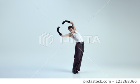 Graceful, young man arching arms in fluid motion with confident stance, blending glamour and movement against white studio background. 123268366