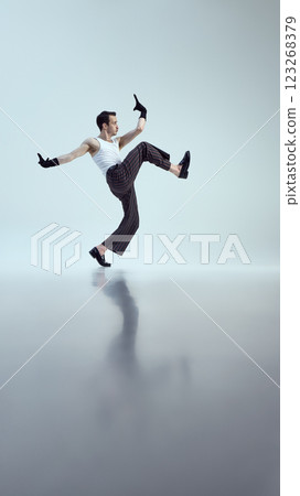 Dynamic performer, dressed stylish attire, leaping mid-air with strong posture and expressive hand moves against white studio background. 123268379