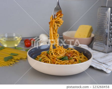 Fork lifting balanesi pasta with tomato sauce over a bowl, with ingredients and kitchen utensils in the background, creating a delicious and inviting culinary scene 123268458