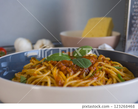 Rustic ceramic bowl holding balanesi pasta garnished with fresh basil, surrounded by cooking ingredients and kitchen tools 123268468