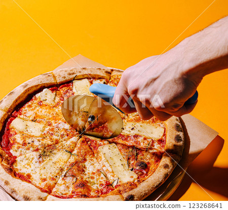 Hands using a pizza cutter on freshly baked pizza with cheese Hands using a pizza cutter on freshly baked pizza with cheese 123268641