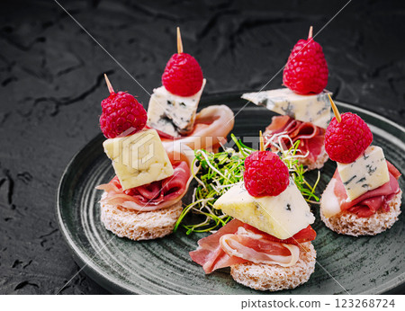 Delicious appetizers with cheese, prosciutto, and raspberries on plate 123268724