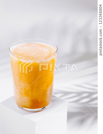 Refreshing mango smoothie standing on white cube with tropical palm leaf shadow 123268804