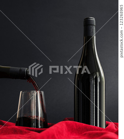 Pouring red wine into a glass beside a bottle on a velvet backdrop Pouring red wine into a glass beside a bottle on a velvet backdrop 123268965