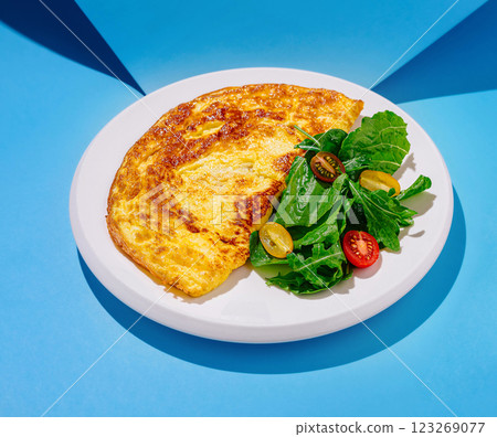 Delicious omelet served with fresh salad on vibrant blue background Delicious omelet served with fresh salad on vibrant blue background 123269077