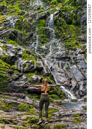 Woman Traveler Standing by Waterfall with Hands Outstretched Woman Traveler Standing by Waterfall with Hands Outstretched 123269687