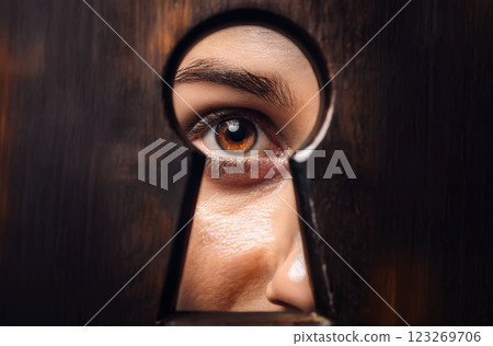 Hidden secrets curiosity or spying concept. Woman eye looking through a keyhole as peeking to see unknown information. Person behind the door sneaks and lurks. Closeup eyeball peering into key hole 123269706