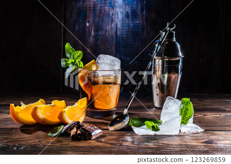 A glass of whiskey and a large ice cube. Steel shaker and bartender's spoon. Sliced citrus and mint. A glass of whiskey and a large ice cube. Steel shaker and bartender's spoon. Sliced citrus and mint. 123269859