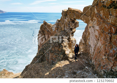 A young woman at a stone arch in the rock with a beautiful view of Lake Baikal in spring. Ice melting time.  123270602
