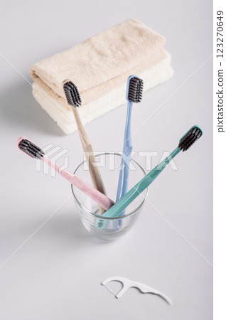 Toothbrushes in a transparent glass and a stack of towels on a gray background vertical view 123270649