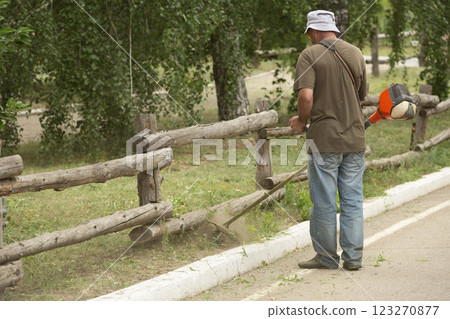 Worker mows grass with a petrol trimmer in a city park. The process of mowing a lawn with a manual lawn mower. Gardening tools and equipment Worker mows grass with a petrol trimmer in a city park. The process of mowing a lawn with a manual lawn mower. Gardening tools and equipment 123270877