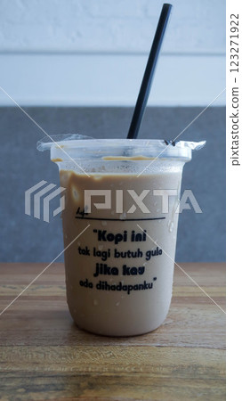 A plastic cup of take away coffee and a straw with a romantic quote to make your day, translate from Indonesian: This coffee no longer needs sugar if you are in front of me. 123271922
