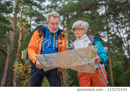 Hiking tourism. Senior couple man woman looking track in paper map enjoying hiking in forest. Happy old people backpackers hikers enjoy walking hike trekking tourism active vacation beauty of nature 123272439