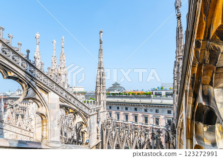 The ornate rooftop of Milan's Duomo features intricate spires and statues under a clear blue sky, showcasing Gothic architecture and offering a unique perspective of the city. 123272991