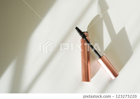 A rose gold mascara tube with its wand slightly angled rests on a clean, minimalist surface A rose gold mascara tube with its wand slightly angled rests on a clean, minimalist surface 123273220