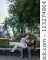 Happy couple in love enjoying a playful moment in the city park. A young man sitting on a bench holding his girlfriend in his arms as they smile at each other. Urban nature, romance, and joy. 123274864