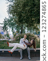 Happy couple in love enjoying a playful moment in the city park. A young man sitting on a bench holding his girlfriend in his arms as they smile at each other. Urban nature, romance, and joy. 123274865