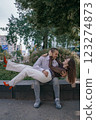 Happy couple in love enjoying a playful moment in the city park. A young man sitting on a bench holding his girlfriend in his arms as they smile at each other. Urban nature, romance, and joy. 123274873