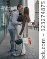 Romantic couple embracing and sharing a kiss in an urban setting. Young stylish man and woman in trendy outfits enjoying a moment of love on a city sidewalk. Modern architecture in the background. 123274875