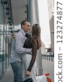 Romantic couple embracing and sharing a kiss in an urban setting. Young stylish man and woman in trendy outfits enjoying a moment of love on a city sidewalk. Modern architecture in the background. 123274877