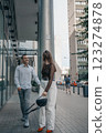 Romantic couple embracing and sharing a kiss in an urban setting. Young stylish man and woman in trendy outfits enjoying a moment of love on a city sidewalk. Modern architecture in the background. 123274878