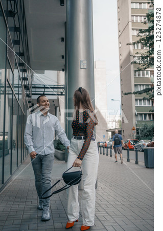 Romantic couple embracing and sharing a kiss in an urban setting. Young stylish man and woman in trendy outfits enjoying a moment of love on a city sidewalk. Modern architecture in the background. 123274878