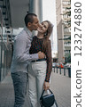 Romantic couple embracing and sharing a kiss in an urban setting. Young stylish man and woman in trendy outfits enjoying a moment of love on a city sidewalk. Modern architecture in the background. 123274880