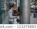 Romantic couple embracing and sharing a kiss in an urban setting. Young stylish man and woman in trendy outfits enjoying a moment of love on a city sidewalk. Modern architecture in the background. 123274883
