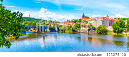 A vibrant view capturing the historic Prague Castle and Manes Bridge on a sunny day with clear skies, overlooking the calm Vltava River. 123275420