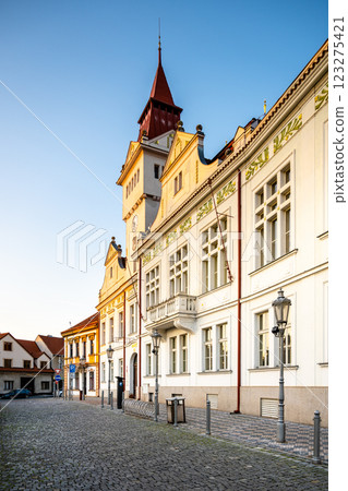 The historic Town Hall in Stara Boleslav stands proudly in the early morning light, showcasing its remarkable architecture along a quiet cobblestone street lined with trees. 123275421