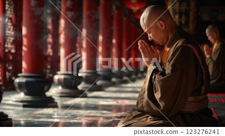 monk bowing in prayer within a sunlit temple adorned with red pillars, symbolizing spirituality, tranquility, and devotion 123276241