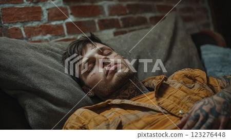 man with face tattoos relaxes peacefully on a cozy couch, eyes closed in a serene moment of rest, surrounded by a warm, rustic setting 123276448
