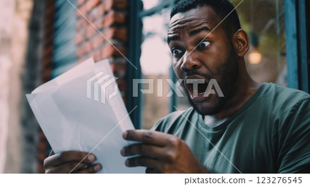 man is captured mid-expression, astonished and shocked while reading an unexpected letter. His wide-eyed reaction conveys a sense of surprise and disbelief 123276545