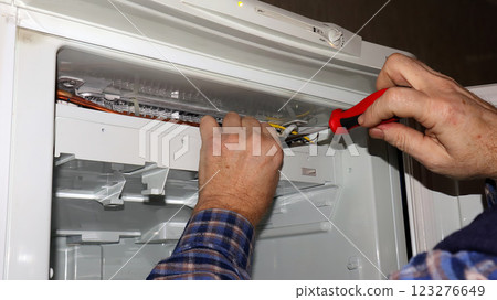 Refrigerator repair expert fixing wiring issues in the appliance during a home service call 123276649